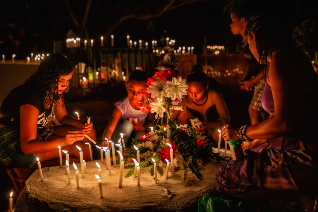 Mulheres e crianças acendem velas durante celebração noturna no cemitério das Cabeceiras, em Juazeiro do Norte.