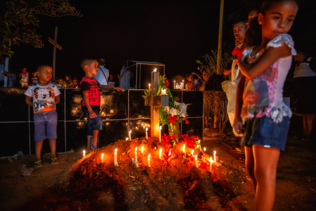 Família observa túmulo iluminado por velas durante celebração noturna no cemitério das Cabeceiras, em Juazeiro do Norte.