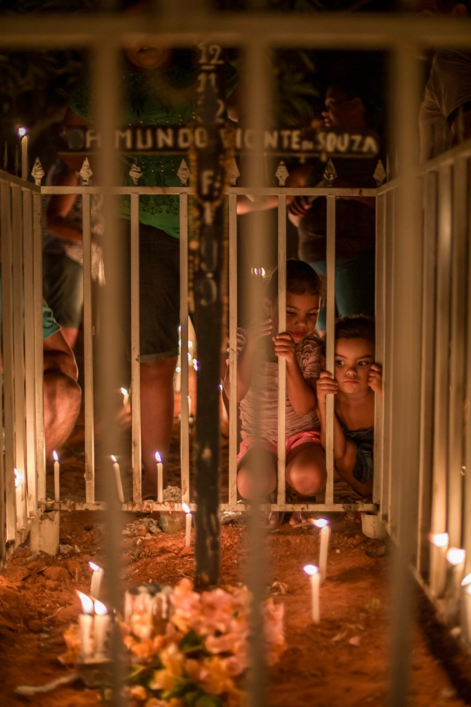 Duas crianças observam túmulo cercado por velas e flores no cemitério das Cabeceiras, em Juazeiro do Norte.
